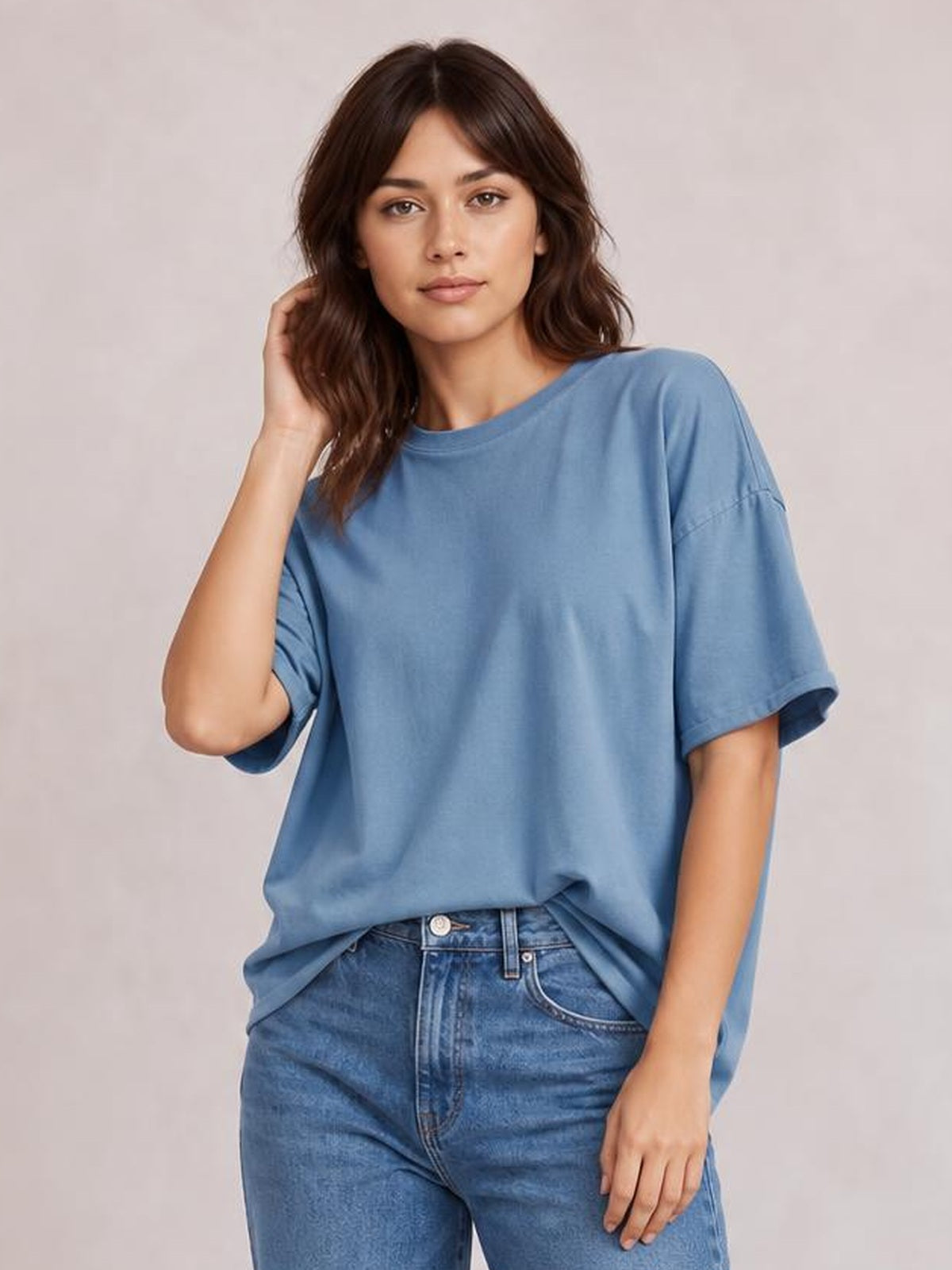 Model wearing a blue exposed seam round neck half sleeve T-shirt with a relaxed silhouette, rolled sleeve cuffs, and a slight front tuck into jeans.
