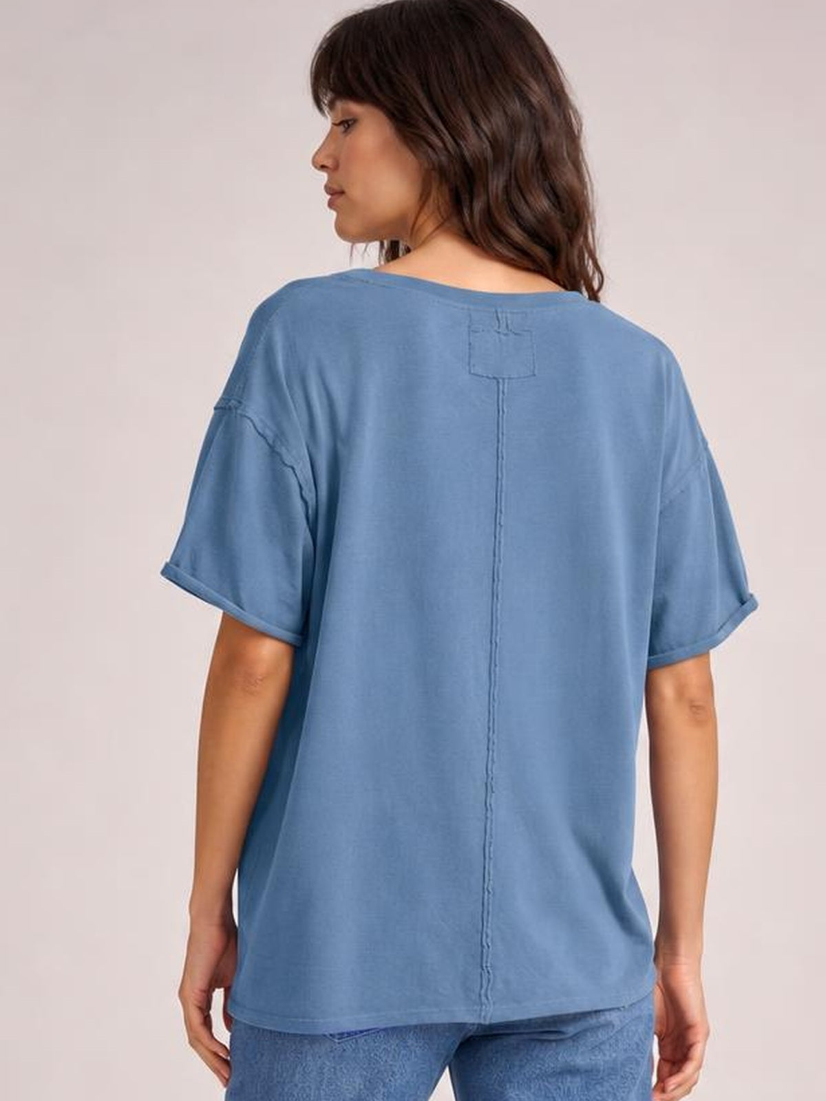 Model shown from the back wearing a blue exposed-seam round-neck half-sleeve T-shirt with a relaxed silhouette and rolled cuffs.