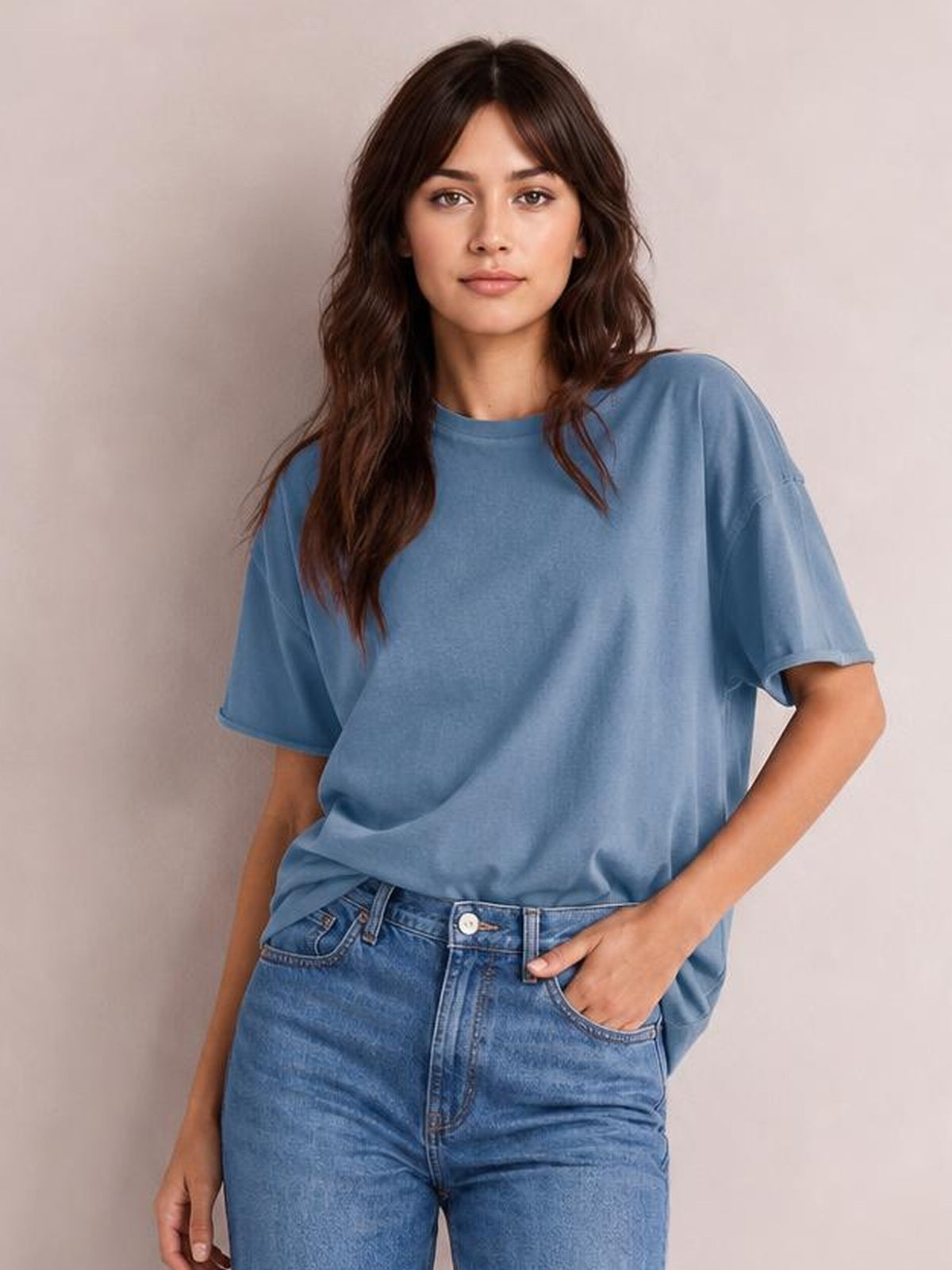 Model wearing a blue exposed seam round neck half sleeve T-shirt with a relaxed silhouette, standing with one hand in her jeans pocket.