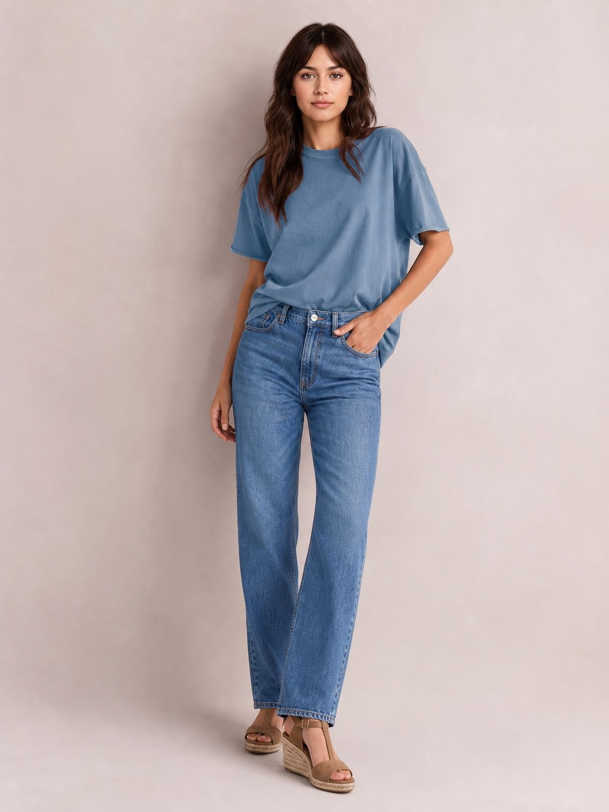 Model wears a blue exposed seam round neck half sleeve T-shirt with a relaxed silhouette, paired with jeans and one hand in a pocket.