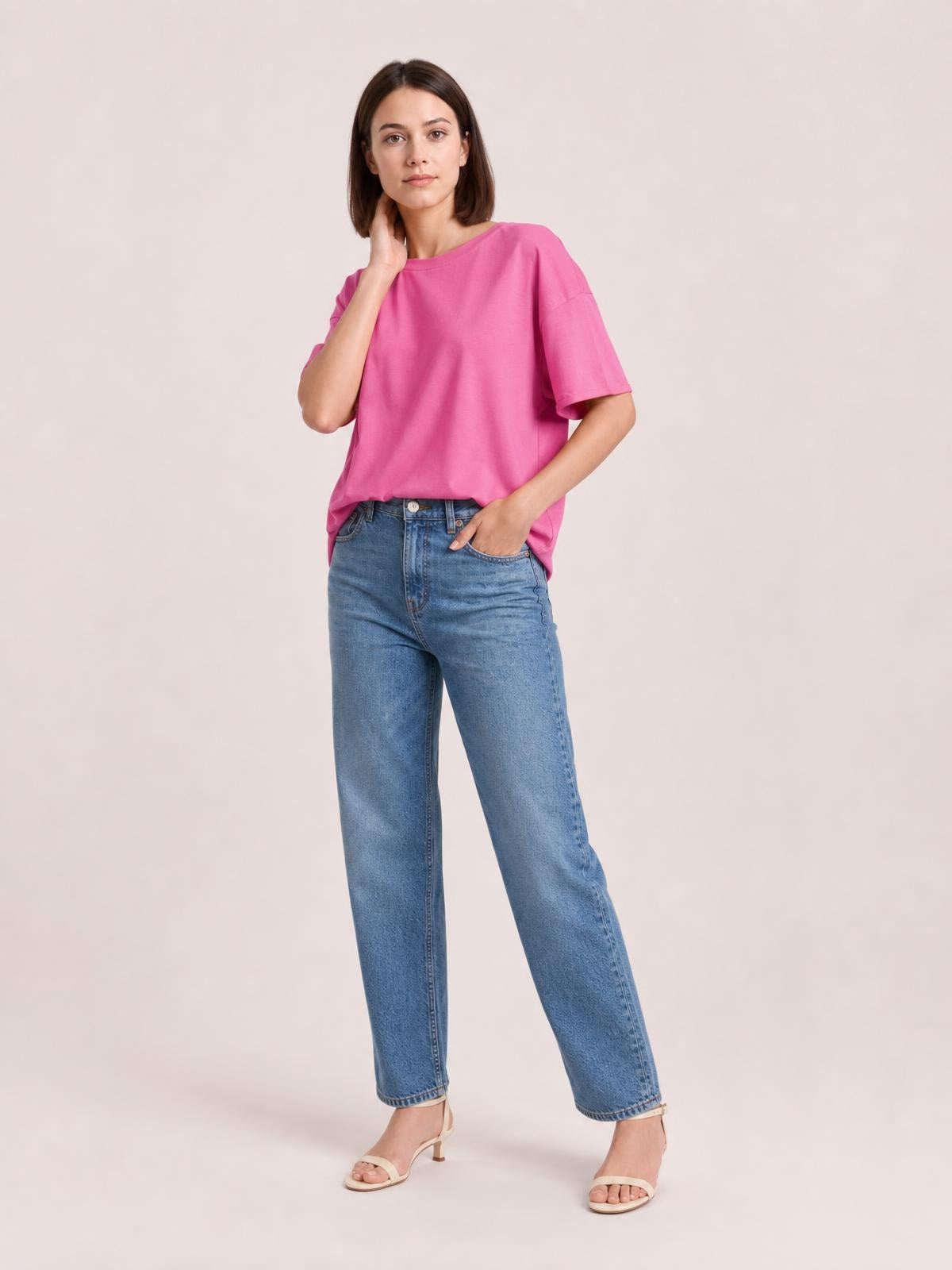 Model wearing a bright pink exposed seam round neck T-shirt with half sleeves and a relaxed silhouette, styled with jeans.