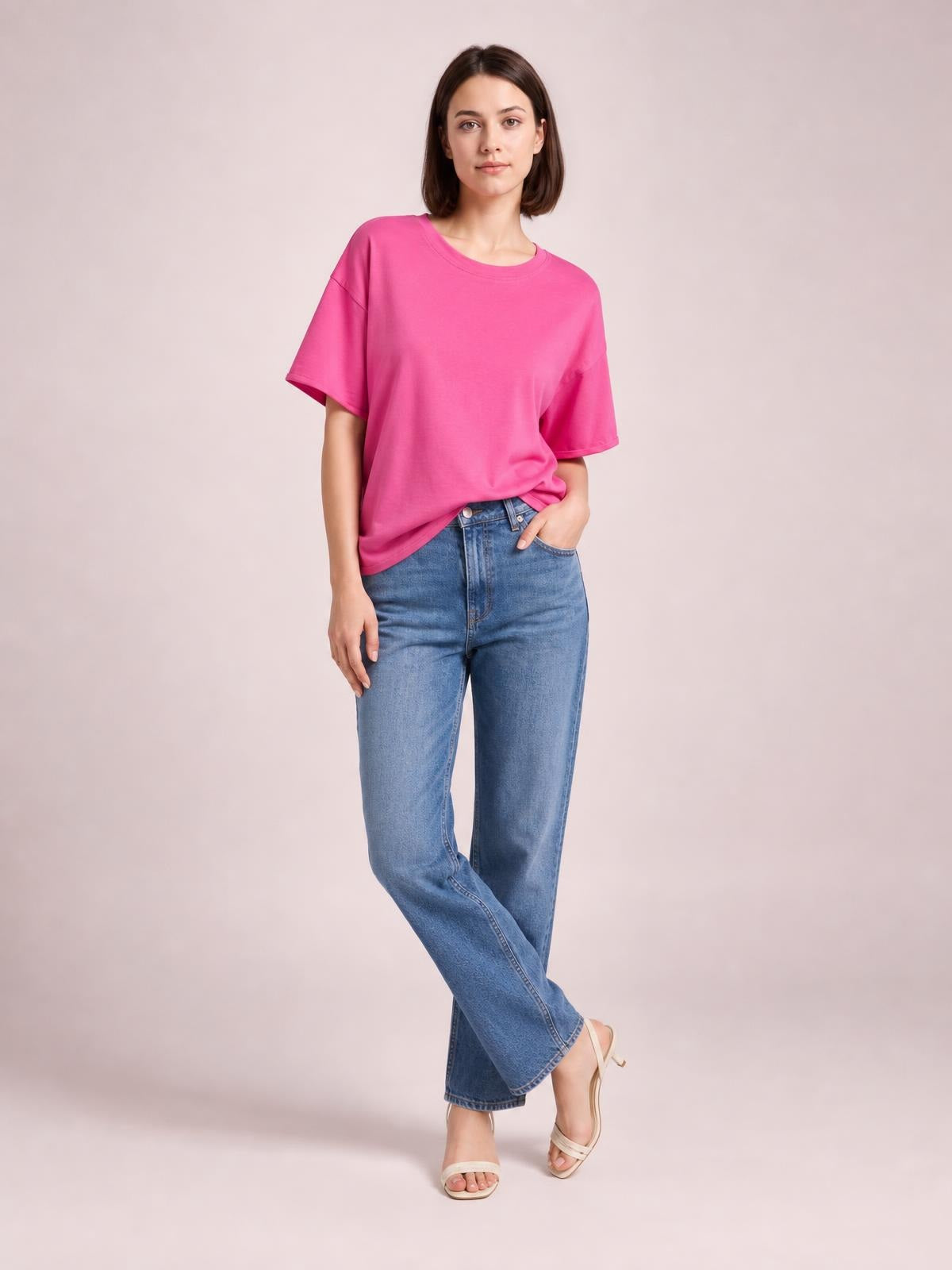A model poses in a bright pink exposed-seam round-neck half-sleeve T-shirt with a relaxed silhouette, paired with jeans and one hand in a pocket.