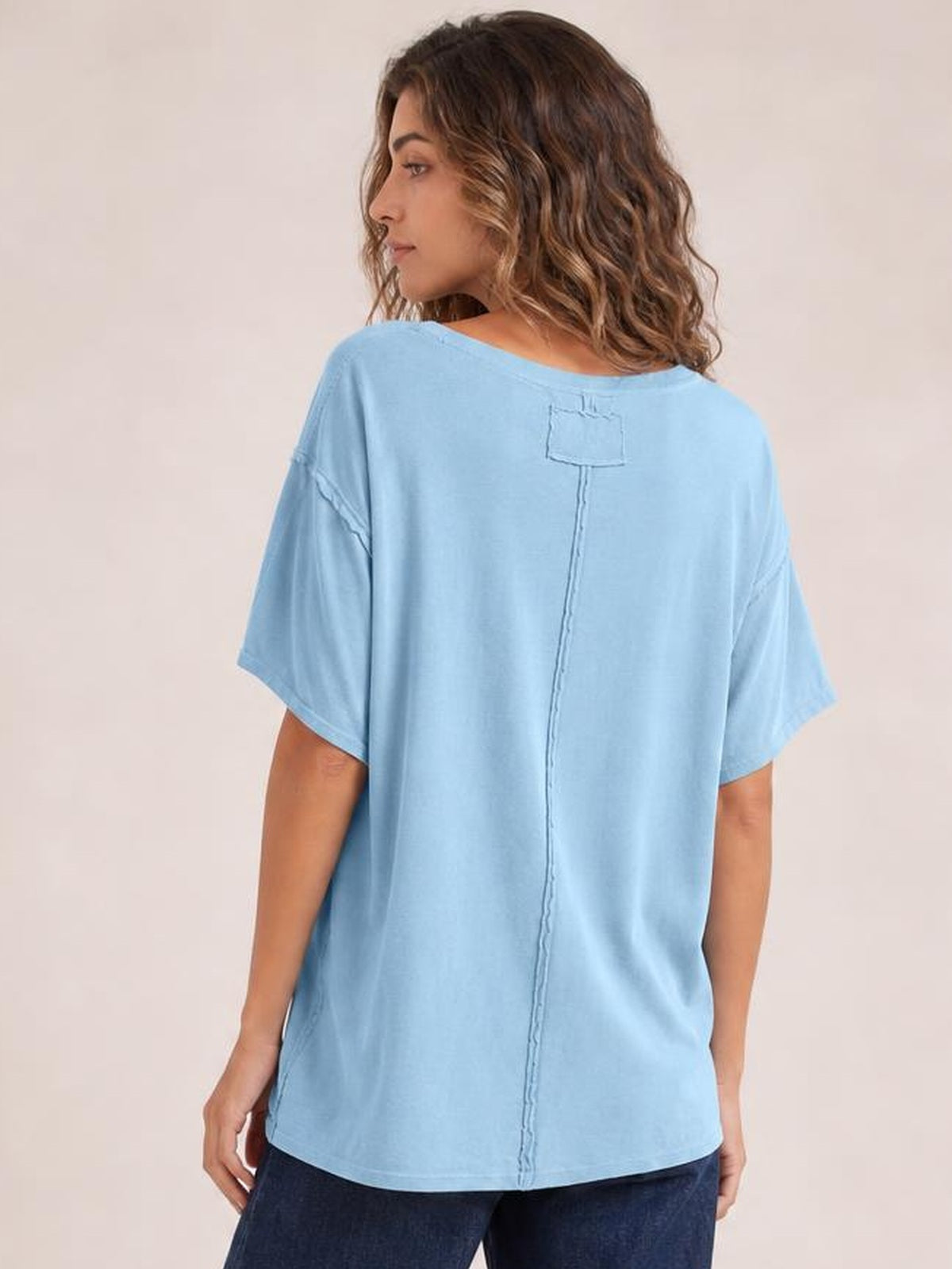Model shown from the back wearing a light blue relaxed-fit round neck T-shirt with half sleeves and exposed center-back and shoulder seams.