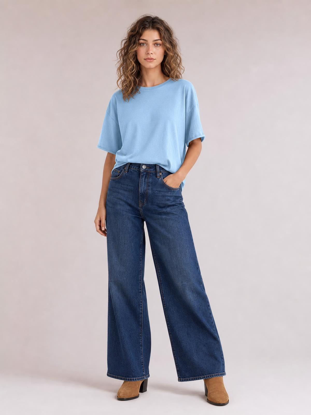 Model poses in a light blue exposed seam round neck half sleeve T-shirt with a relaxed silhouette, paired with wide-leg jeans.