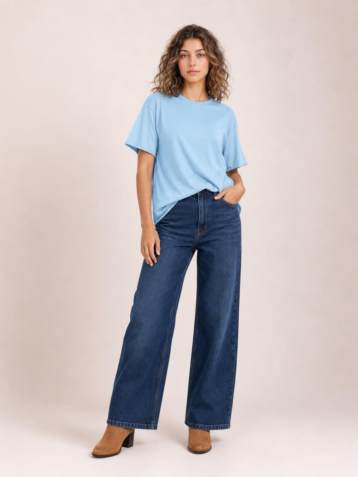 Model wears a light blue exposed seam round neck half sleeve T-shirt with a relaxed silhouette, standing with one hand in her jeans pocket.