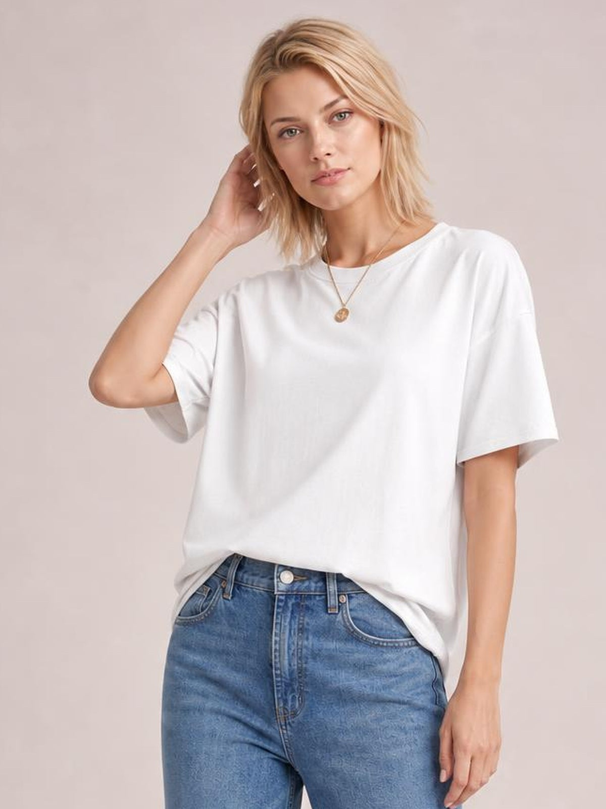 A model poses in a white exposed seam round neck T-shirt with relaxed half sleeves, a loose silhouette, and a slightly tucked hem.