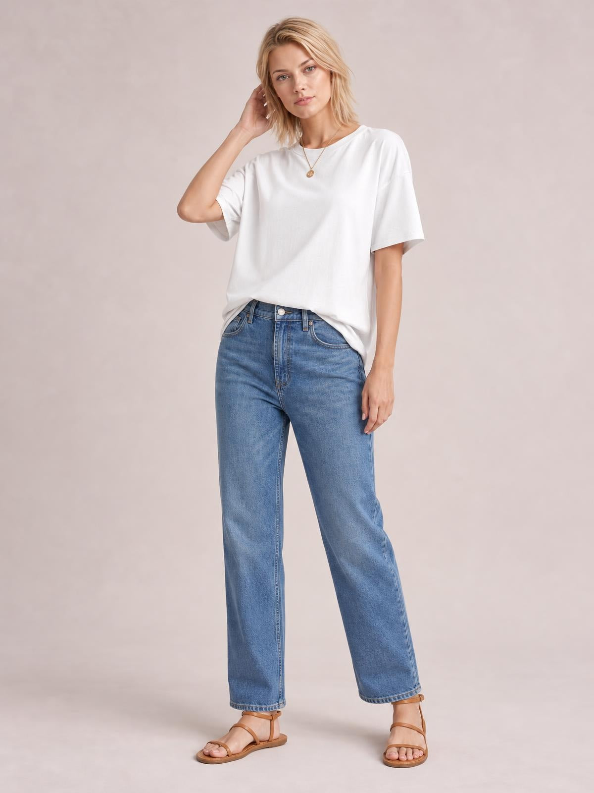 Model wearing a white exposed-seam round-neck T-shirt with relaxed half sleeves and a loose silhouette, posing with one hand touching her hair.