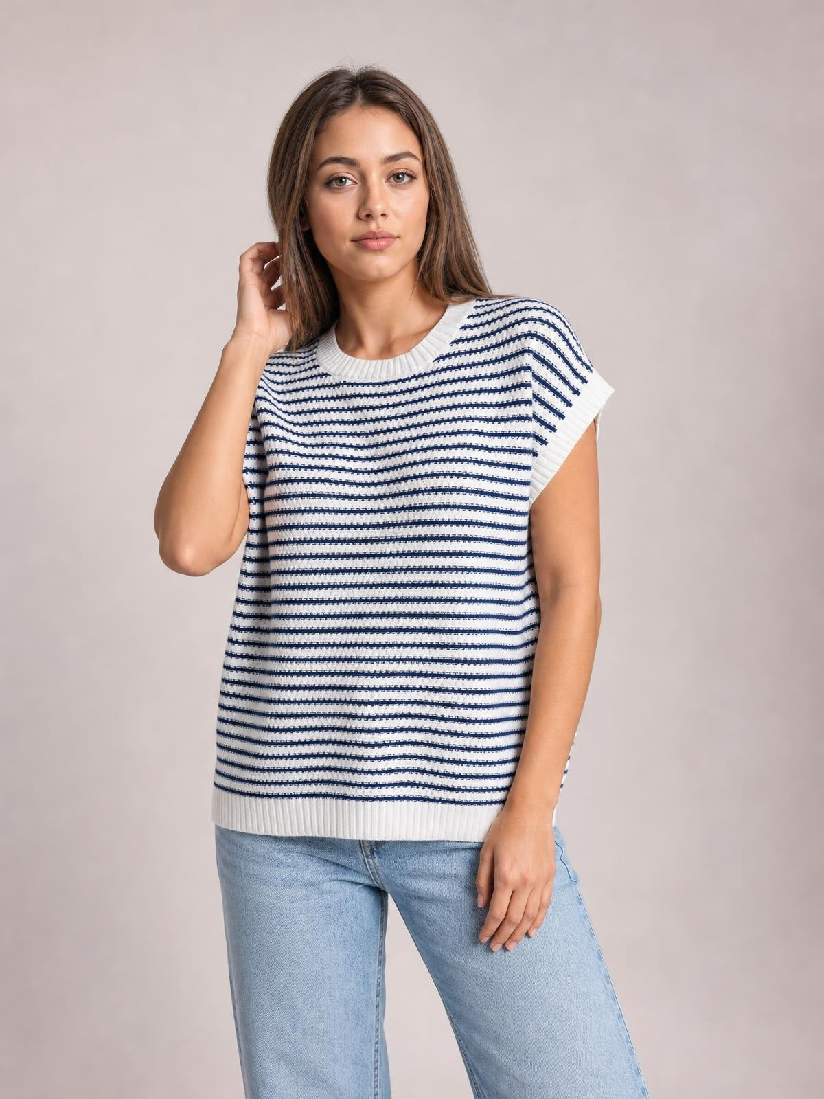 Model wearing a white and navy striped round neck cap sleeve sweater with ribbed trim and a relaxed straight silhouette, posing with one hand near her hair.