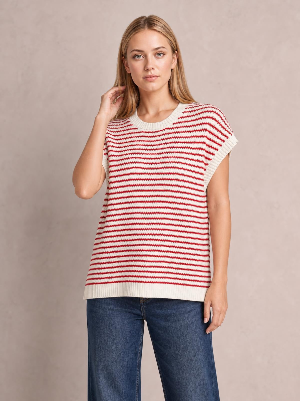 Model wearing a cream and red striped round-neck cap-sleeve sweater with ribbed trim and a relaxed straight silhouette, posing with one hand near her hair.