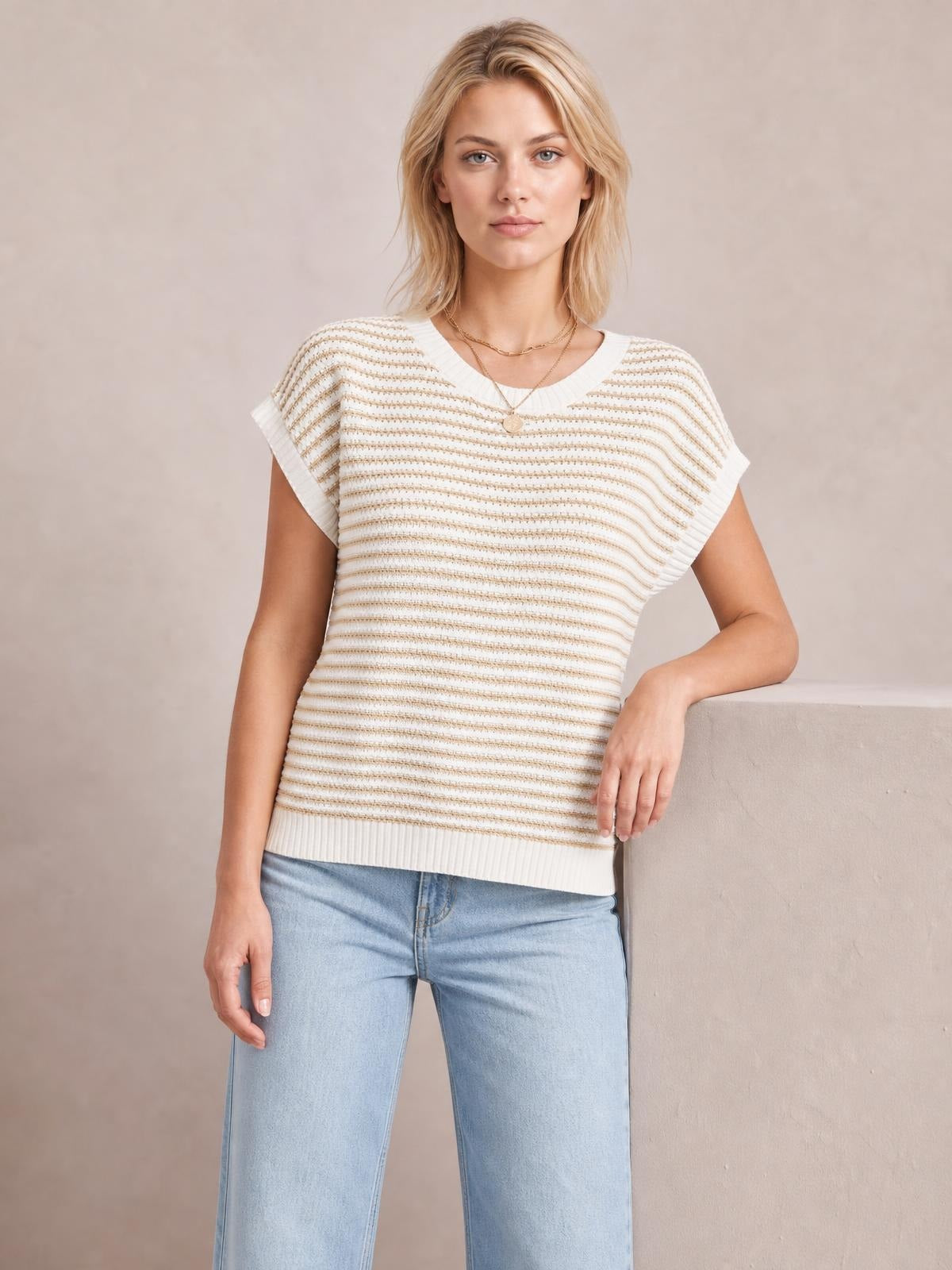 Model wearing a cream striped round neck cap sleeve sweater with a relaxed straight silhouette, ribbed neckline and hem, paired with light wash jeans.