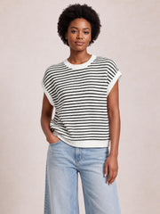 Model wears a black-and-white striped round-neck cap-sleeve sweater with ribbed trim and a relaxed, slightly boxy silhouette, posing with one hand in her pocket.