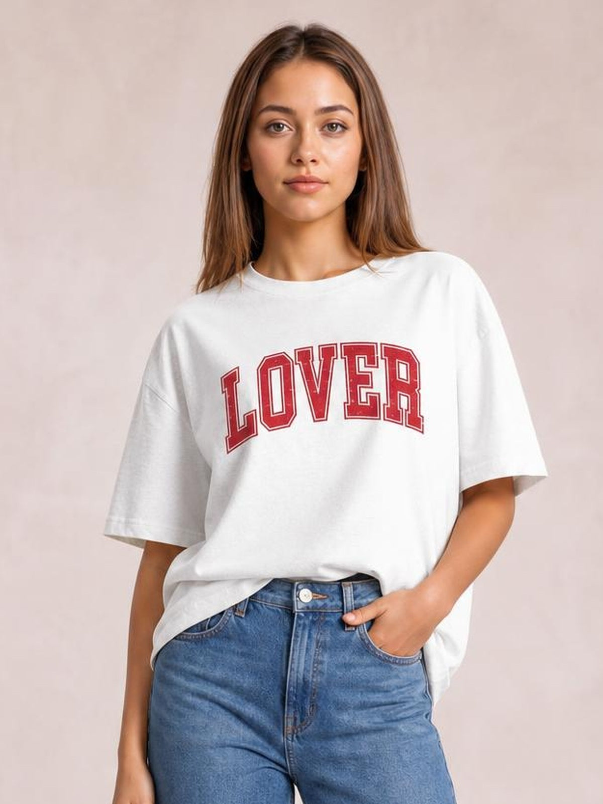 A model wears a white Lover round neck half sleeve T-shirt with a relaxed silhouette, red varsity-style lettering, and one hand in her jeans pocket.