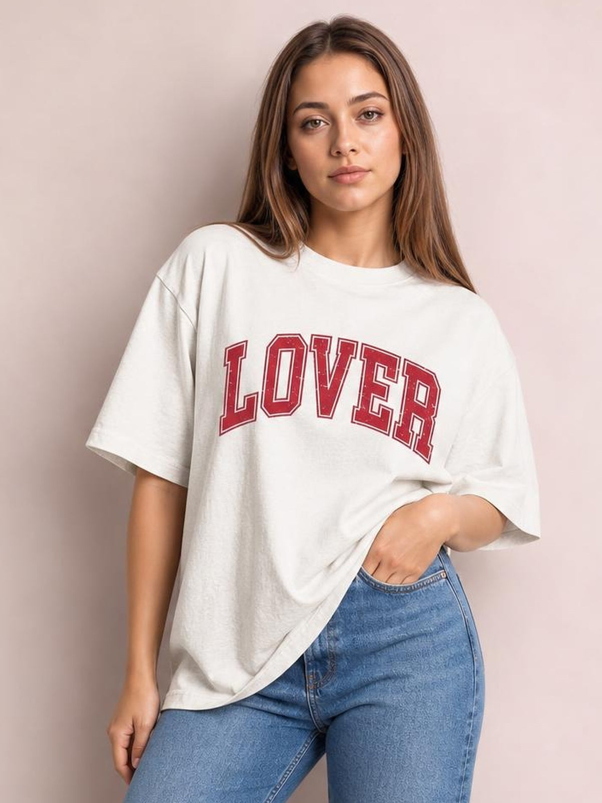 A model poses in a white round neck half sleeve T-shirt with a relaxed oversized silhouette, red LOVER chest lettering, and one hand tucked at her jeans waistband.