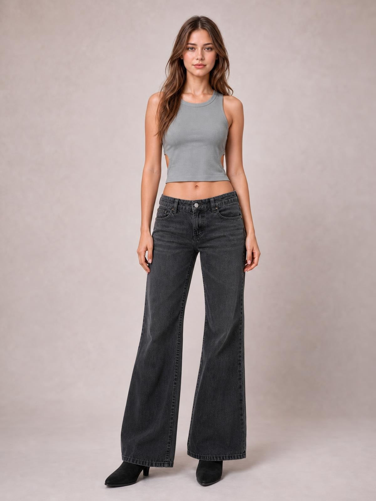 Model standing in dark gray low-rise flare leg jeans with front pockets, belt loops, button closure, and a wide-leg silhouette.