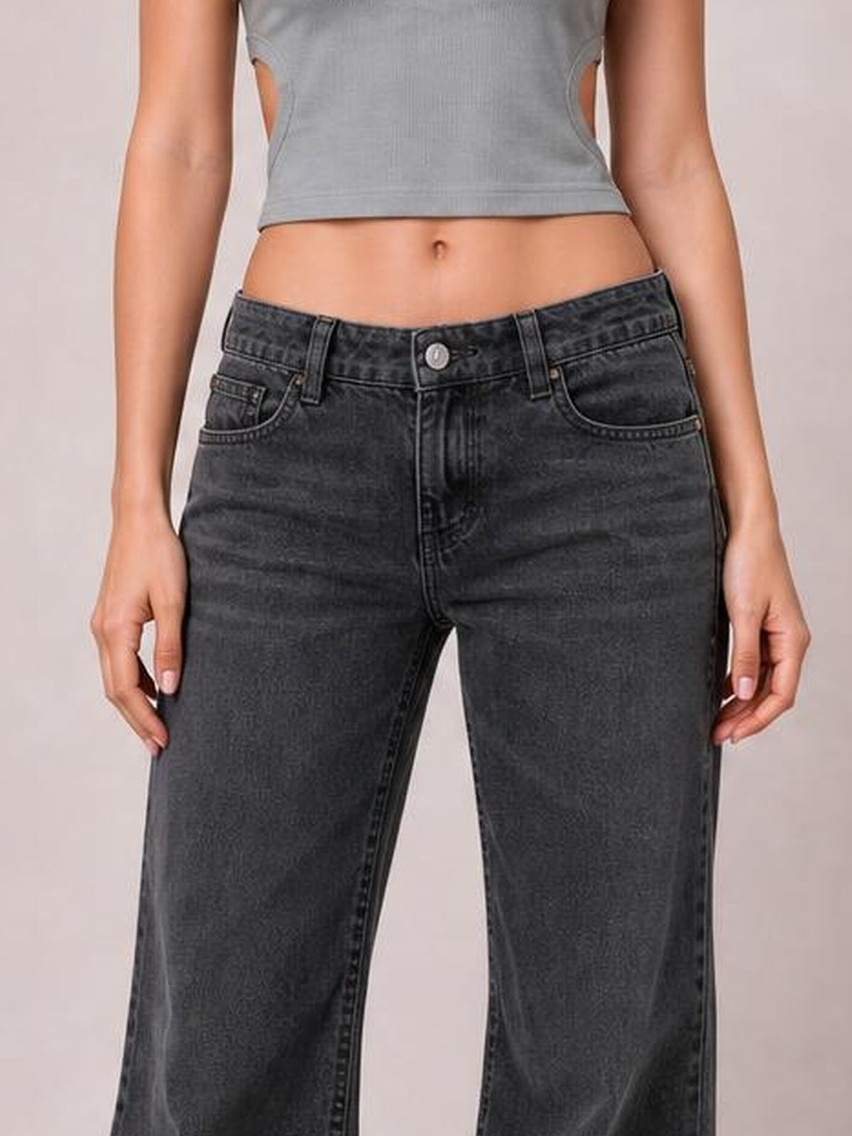 A cropped model wears dark charcoal low-rise flare-leg jeans with a button closure, belt loops, front pockets, and visible contrast stitching.