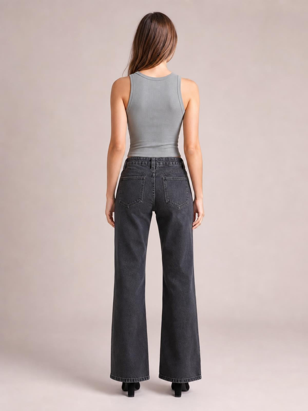 Model viewed from the back wearing dark gray low-rise flare leg jeans with belt loops, buttoned waistband, and two patch back pockets.