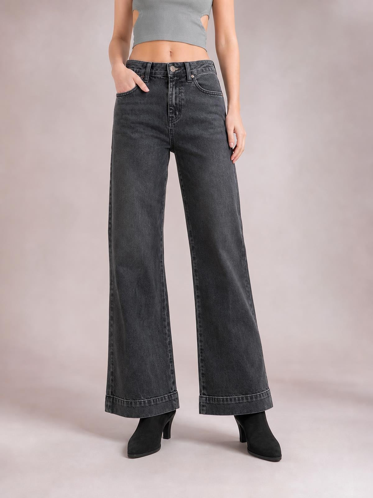 Model stands with one hand in the pocket wearing dark gray low-rise flare leg jeans with belt loops, button closure, front pockets, and wide cuffed hems.