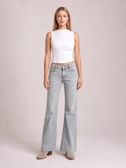 Model stands facing forward in light gray low rise flare leg jeans with front pockets, belt loops, button closure, and a relaxed wide-leg silhouette.