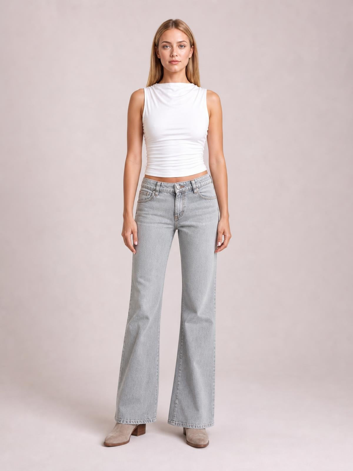 Model stands facing forward in light gray low rise flare leg jeans with front pockets, belt loops, button closure, and a relaxed wide-leg silhouette.