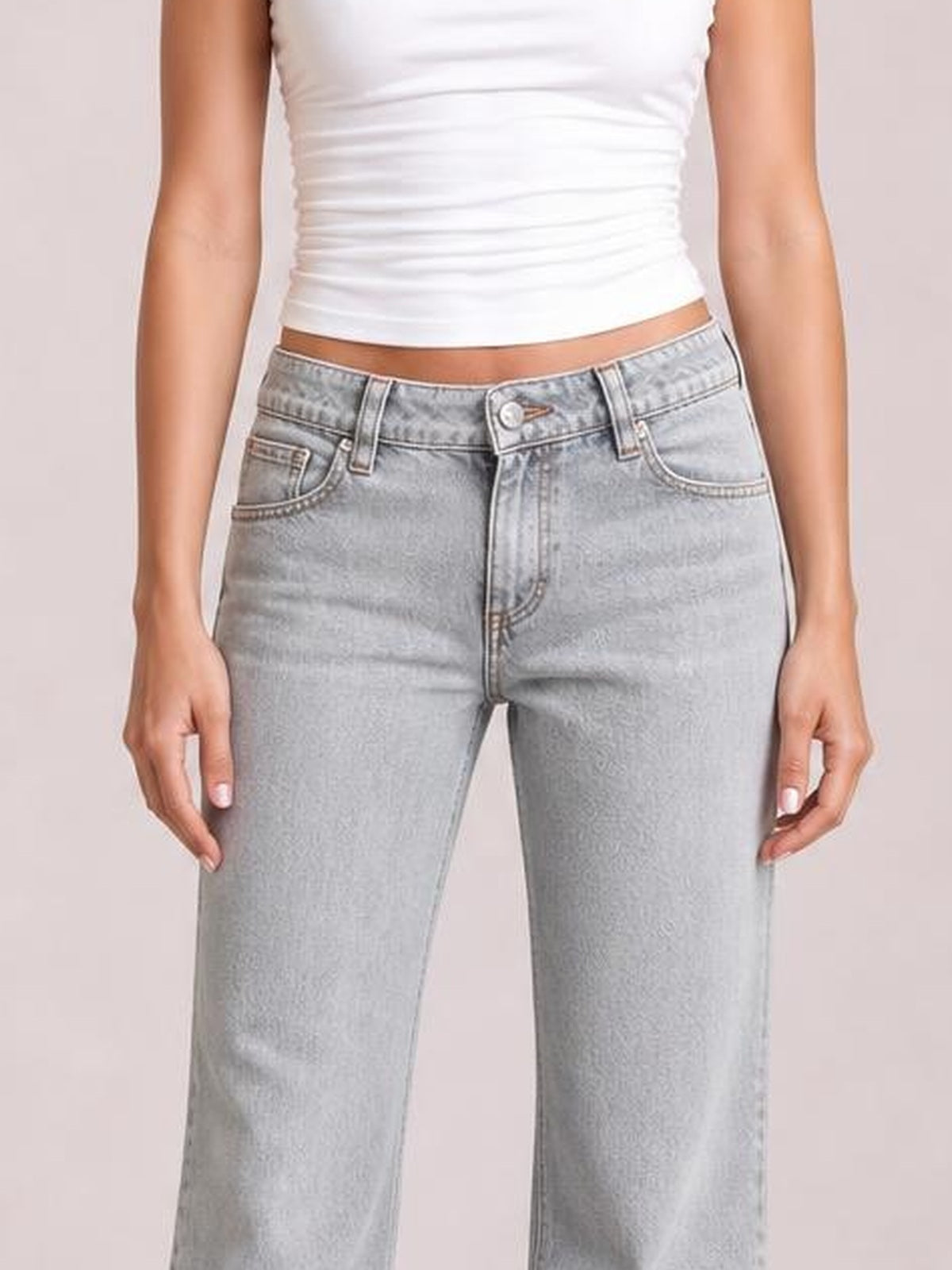 Model wears light gray low-rise flare leg jeans with front pockets, belt loops, button closure, and a structured silhouette while standing with hands at her sides.