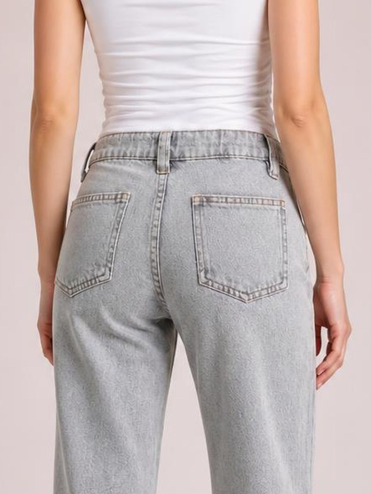 A model stands facing away in light gray low-rise flare leg jeans, showing belt loops, contrast stitching, and two large back patch pockets.