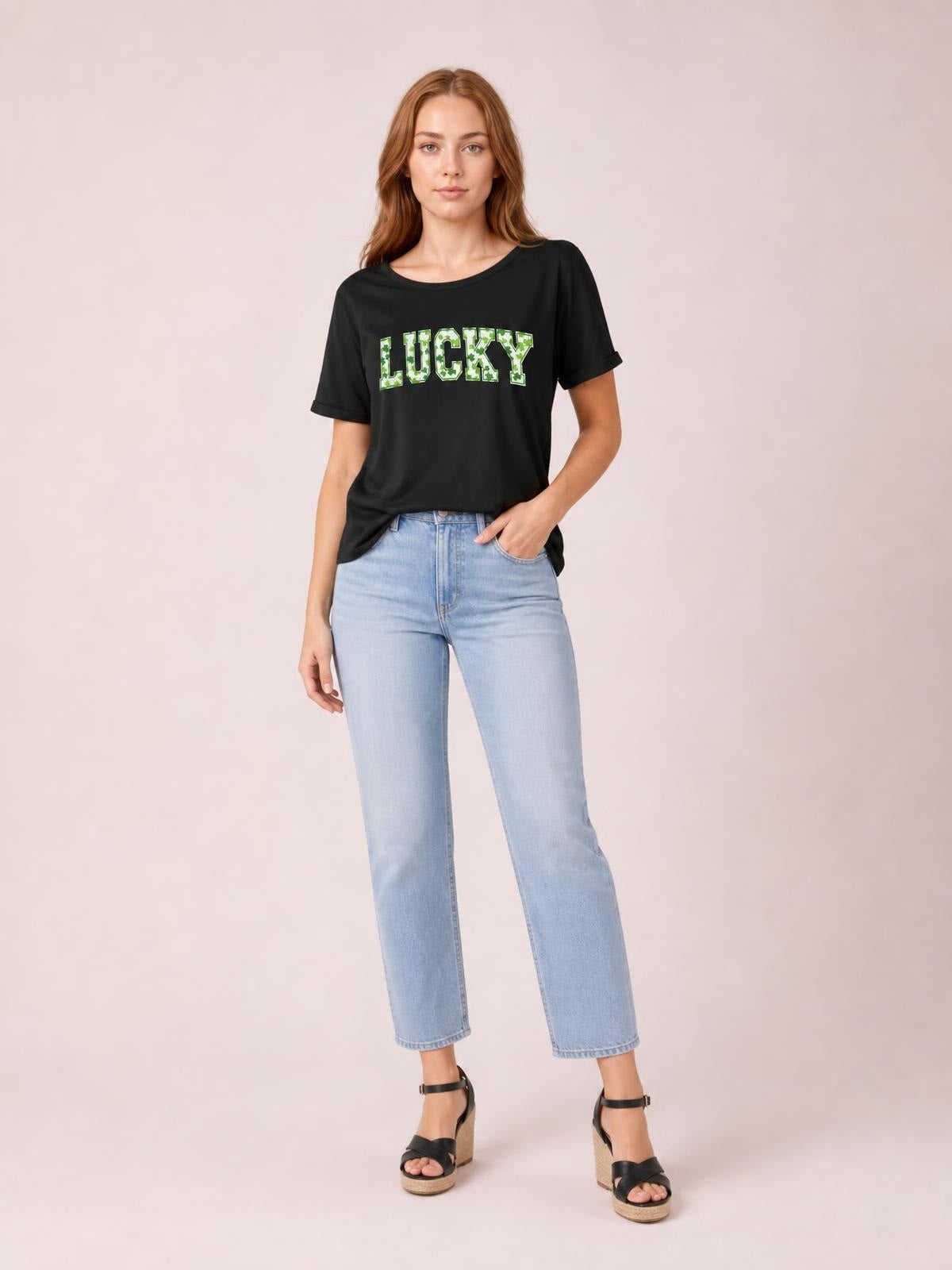 Model wears a black short-sleeve T-shirt with a relaxed silhouette, crew neckline, rolled cuffs, and bold green clover-patterned “LUCKY” lettering.