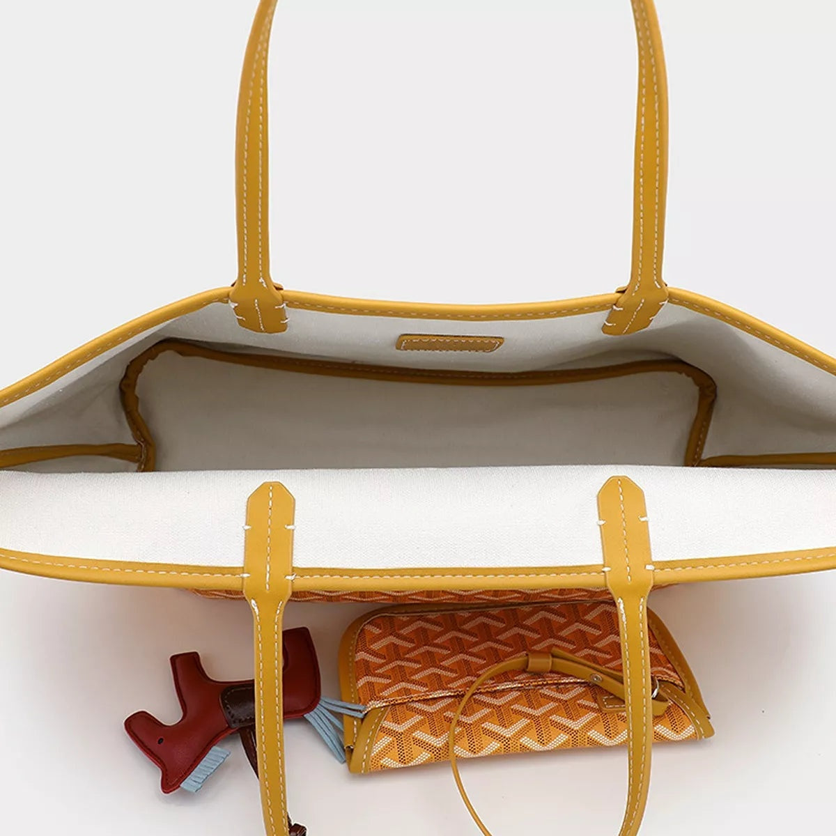 Open large white PU leather tote handbag with mustard-yellow trim and handles, revealing a detachable geometric-pattern pouch and horse charm inside.