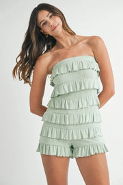 Model poses in a mint pointelle knit tube romper with a strapless silhouette, layered ruffle trim, textured construction, and ruffled shorts.