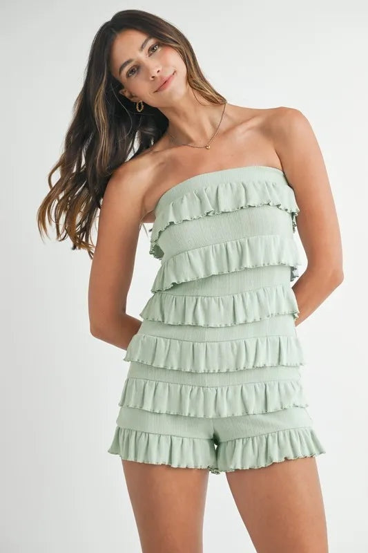 Model poses in a mint pointelle knit tube romper with a strapless silhouette, layered ruffle trim, textured construction, and ruffled shorts.