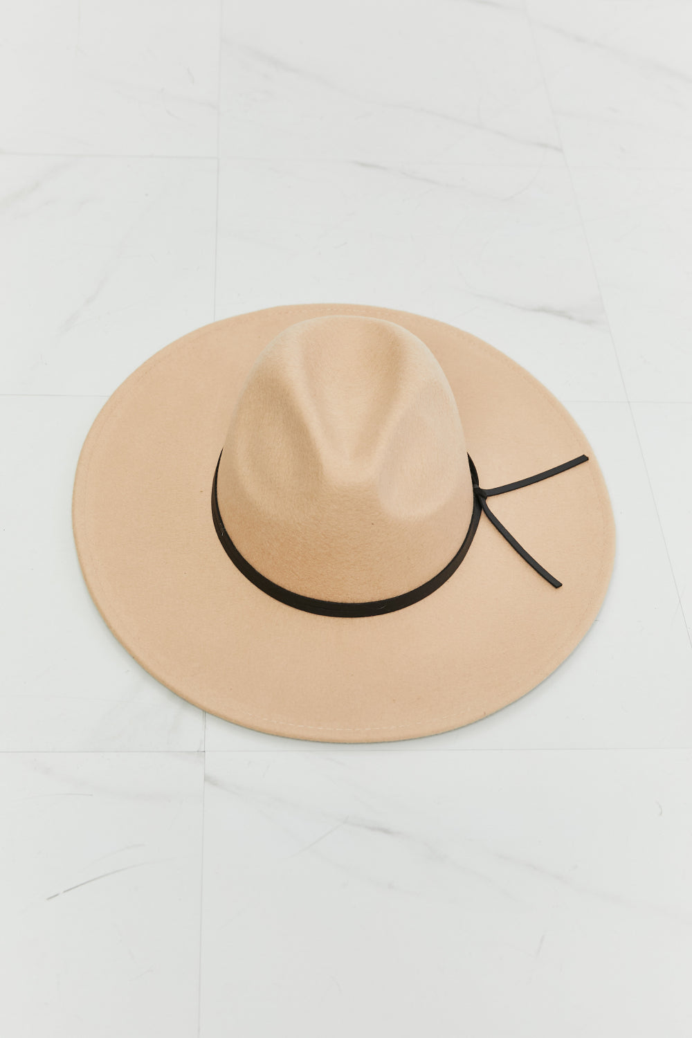 A classic beige fedora hat with a softly structured crown, wide brim, and contrasting black band finished with a tied detail.