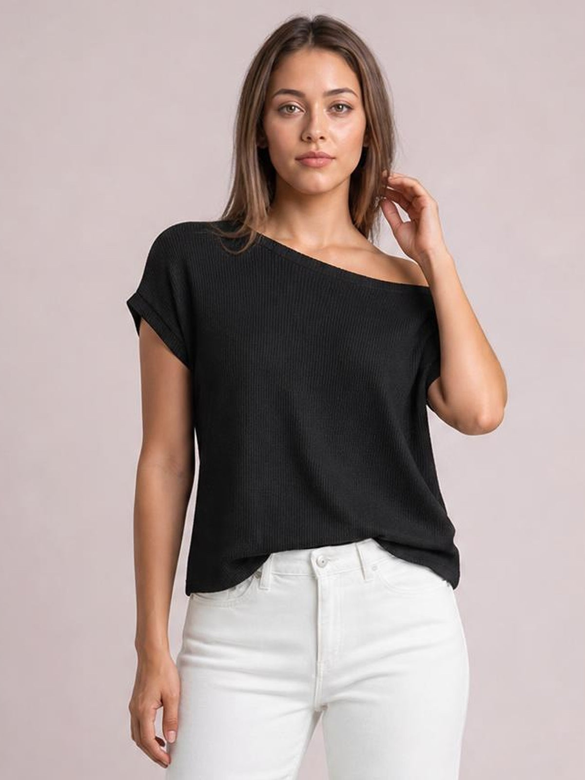 Model wears a black boat neck short sleeve knit top with a relaxed silhouette, rolled cuffs, and a softly draped hem while touching her hair.