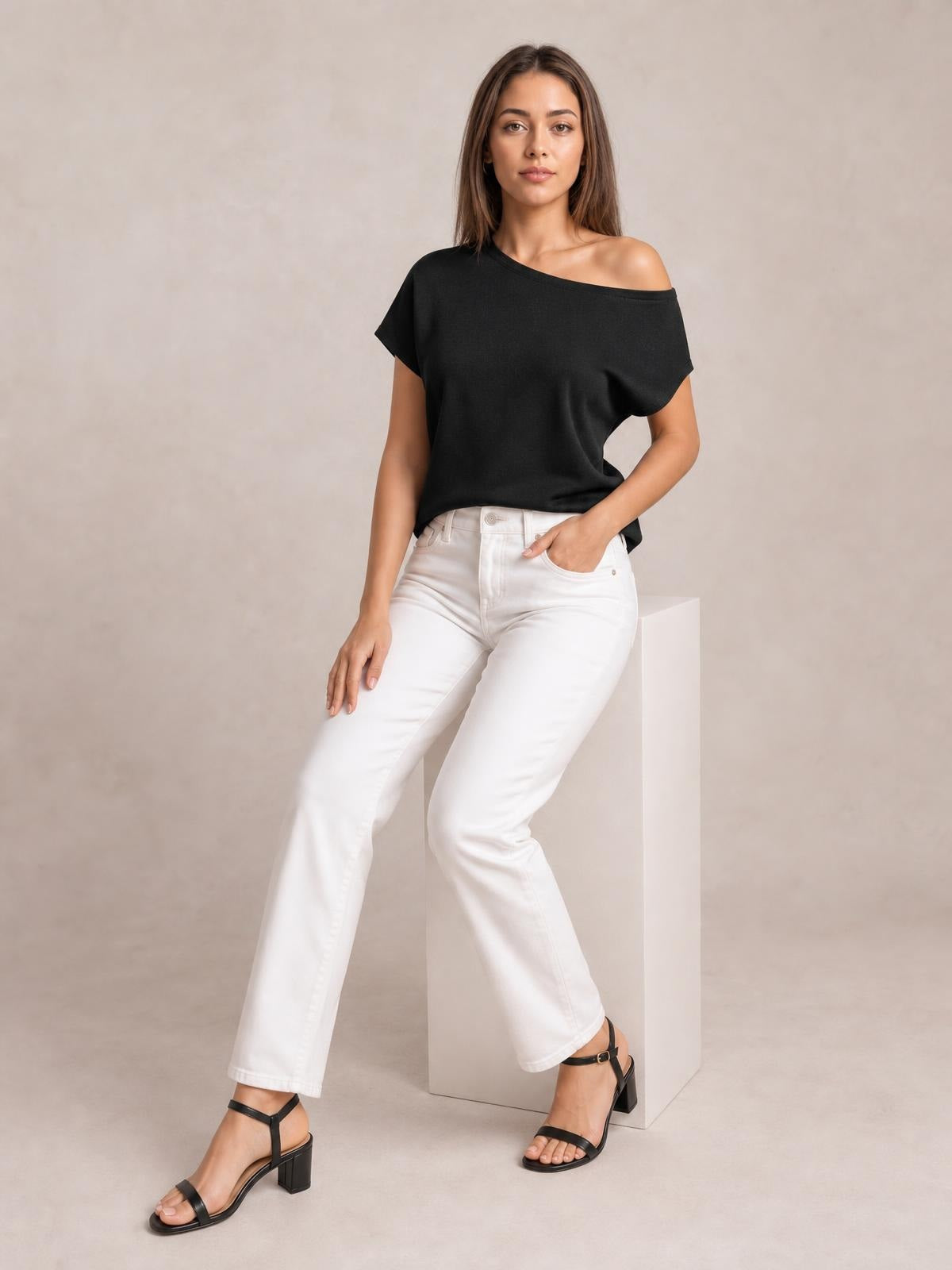 Model wearing a black boat neck short sleeve knit top with a relaxed silhouette, angled neckline, and soft drape, posed with one hand in her pocket.