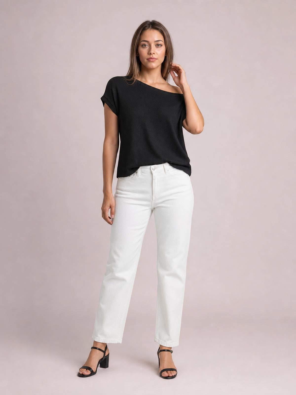 Model poses in a black boat neck short sleeve knit top with a relaxed, boxy silhouette, rolled sleeve cuffs, and curved hem.