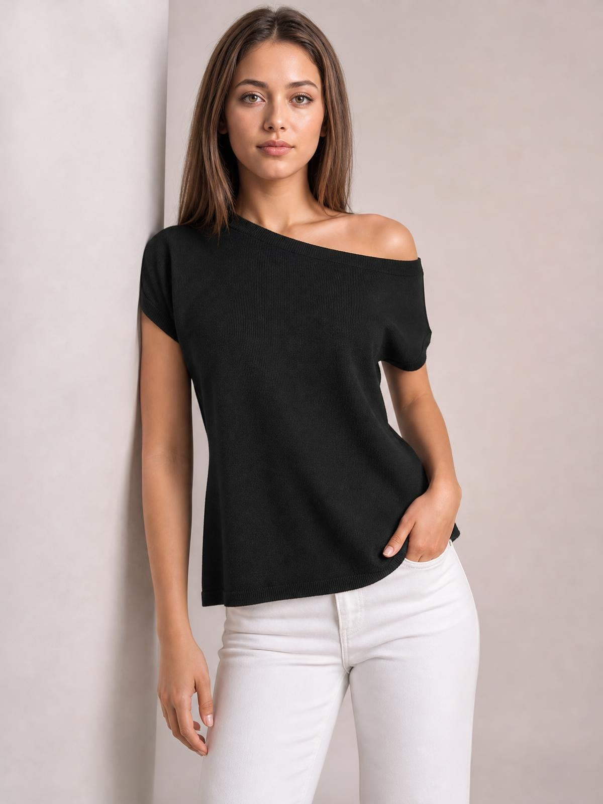 Model wearing a black boat neck short sleeve knit top with a relaxed silhouette, ribbed texture, and straight hem, posing with one hand in her pocket.