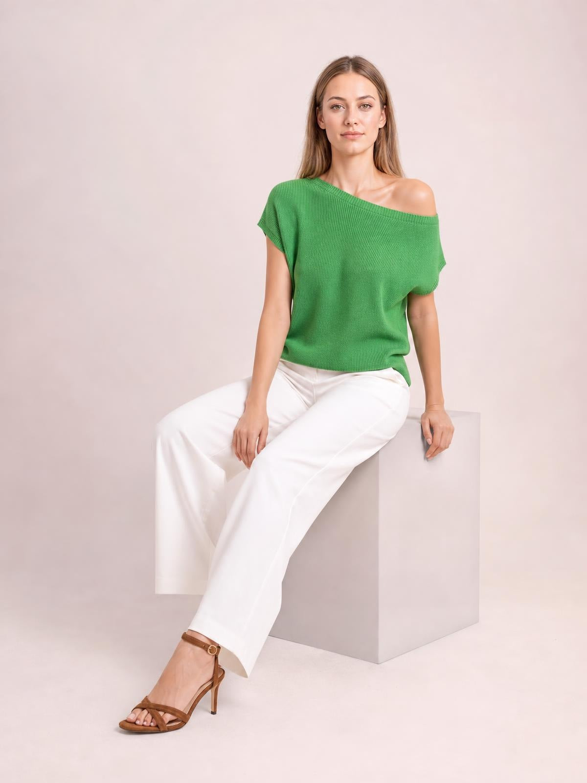 Model seated in a relaxed pose wearing a green boat neck short sleeve knit top with a loose, straight silhouette and wide neckline.