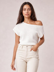 Model wearing a white boat neck short sleeve knit top with a relaxed, draped silhouette and wide neckline, posed with one hand in her pocket.