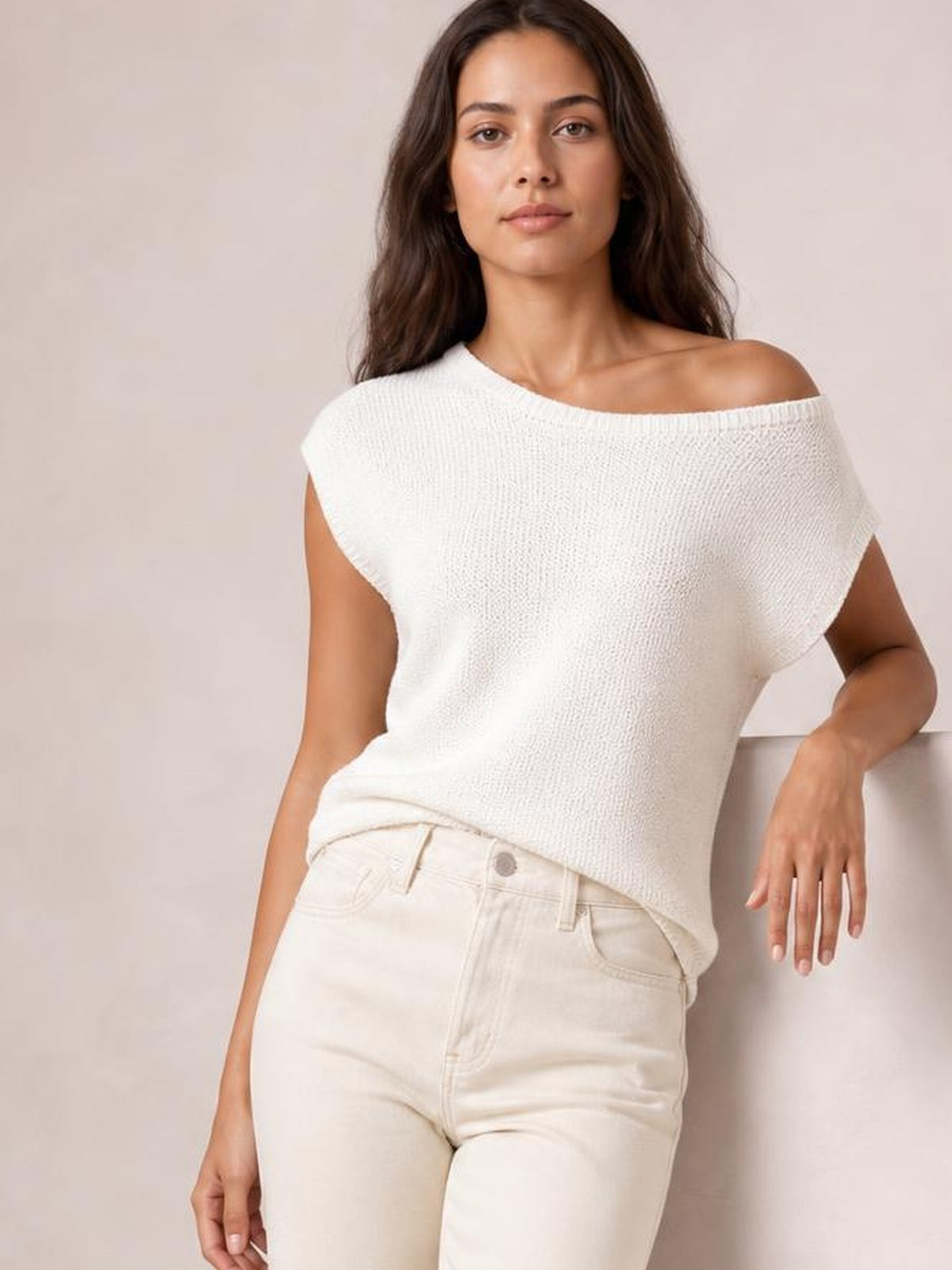 Model wearing a white boat neck short sleeve knit top with a relaxed silhouette and wide neckline, leaning casually with one hand resting at her side.