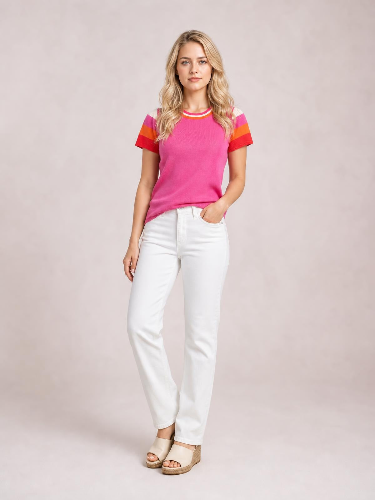 Model wears a pink contrast round-neck short-sleeve knit top with multicolor striped sleeves, a relaxed straight silhouette, and one hand in her pocket.