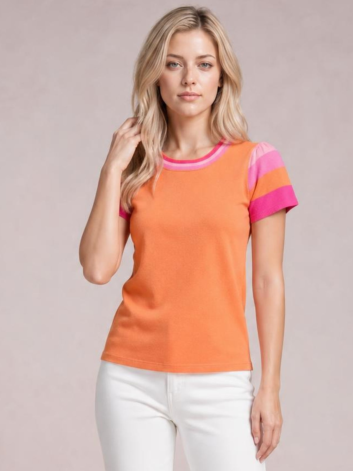 Model poses in an orange contrast round neck short sleeve knit top with pink striped trim, fitted silhouette, and straight hem.