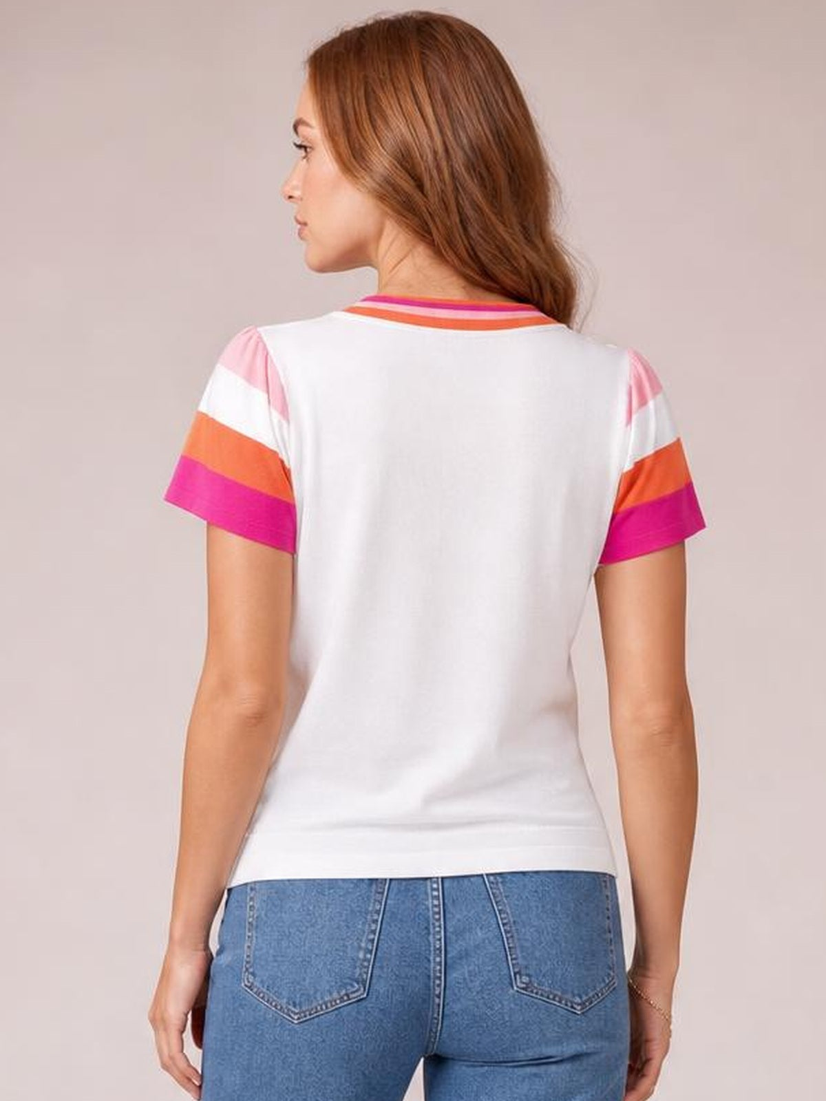 A model stands in a back view wearing a white knit top with a round neck, short sleeves, and bold pink and orange contrast stripes.