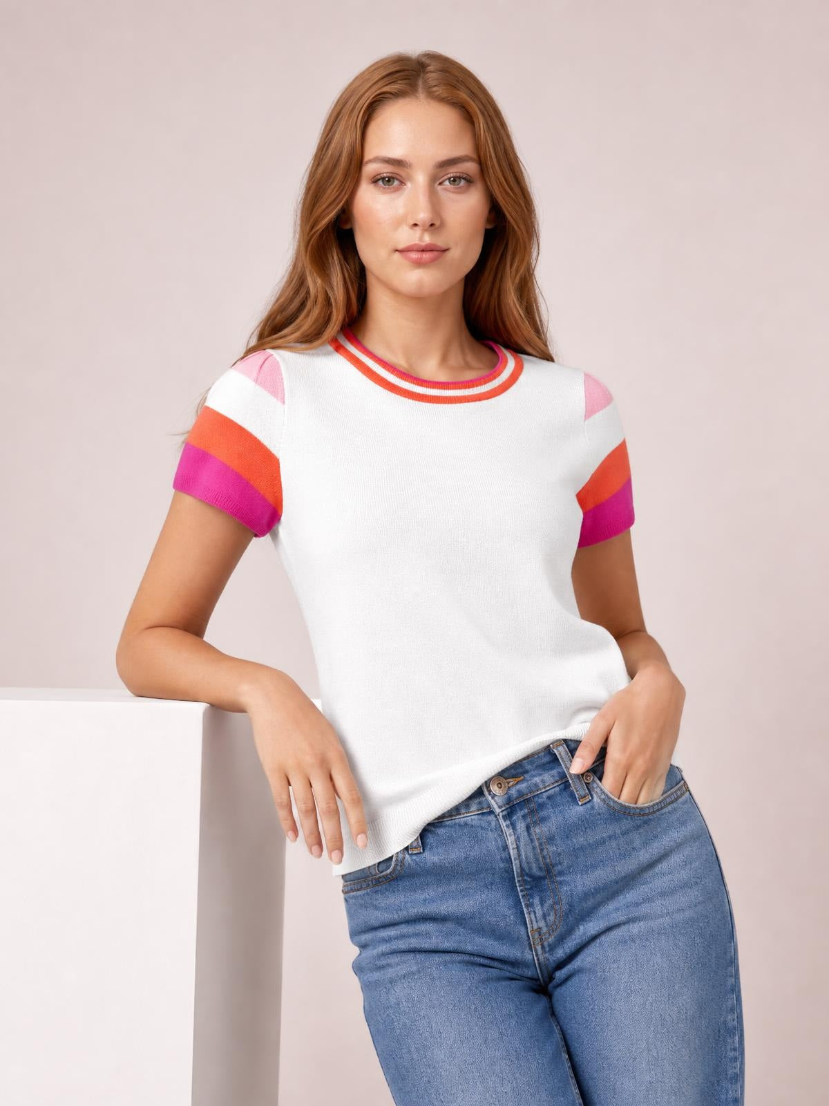 Model poses in a white knit top with a round neck, short sleeves, and pink-and-orange contrast striped trim in a relaxed silhouette.