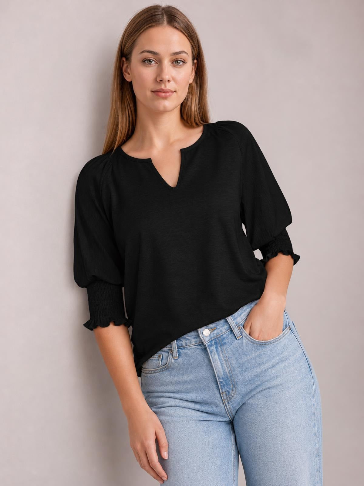 A model poses in a black heathered blouse with a notched neckline, voluminous lantern sleeves, frilled cuffs, and a relaxed silhouette, one hand in her jeans pocket.