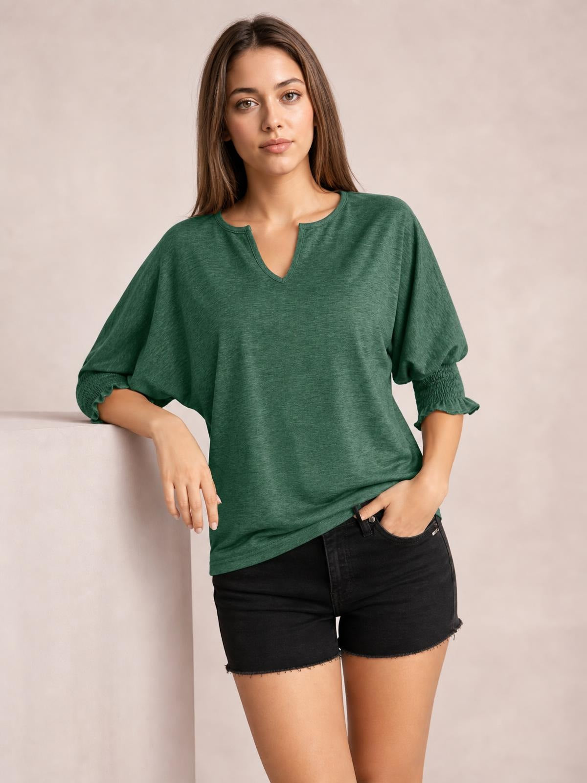Model poses in a heathered green blouse with a notched neckline, loose lantern sleeves, and frill-trimmed cuffs, paired with black shorts.