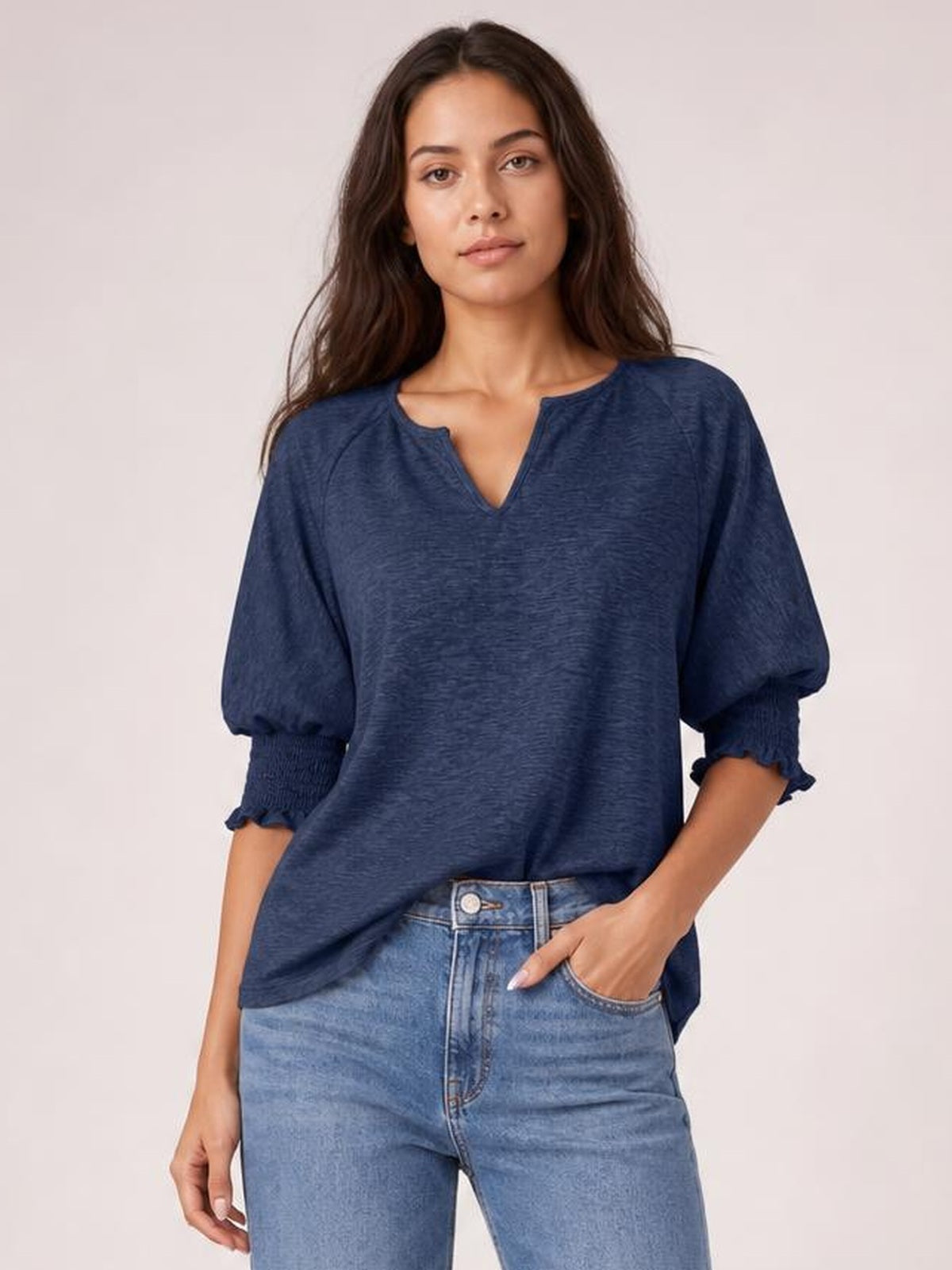 Model wears a heathered navy blouse with a notched neckline, loose silhouette, lantern sleeves, and frill-trimmed cuffs, posing with one hand in her jeans pocket.