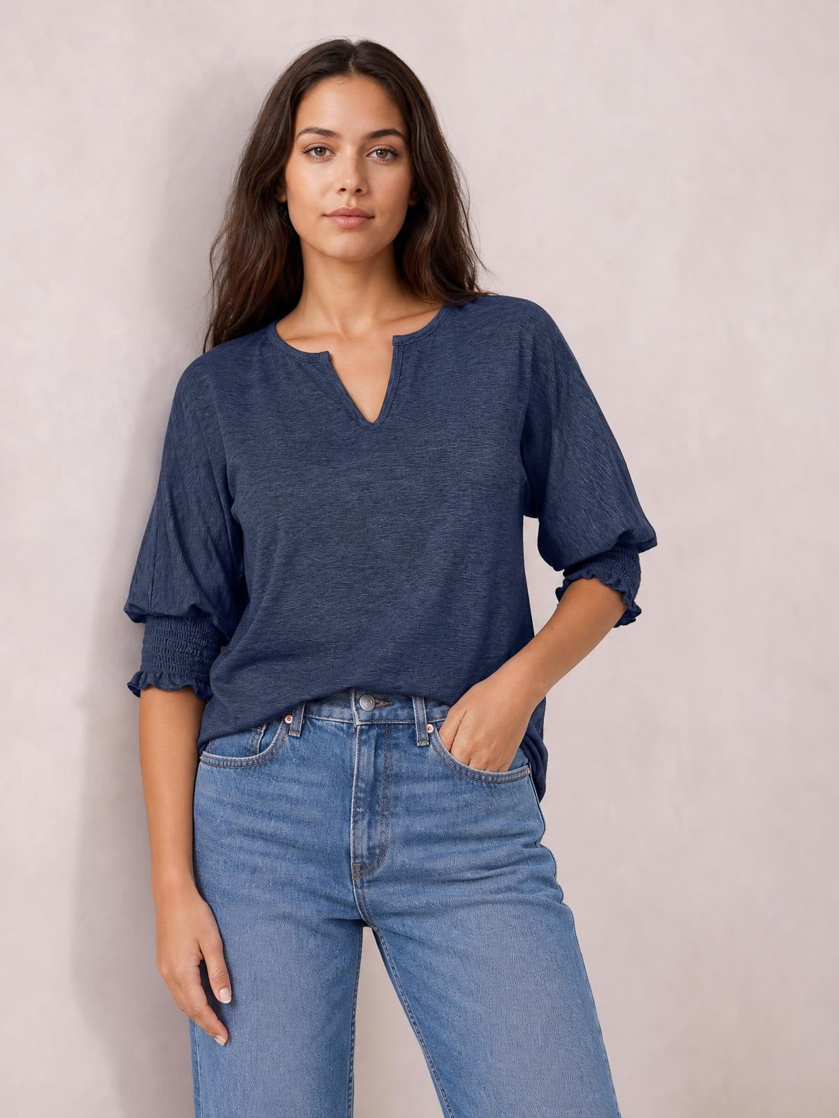 A model poses with one hand in her jeans pocket, wearing a heathered navy blouse with a notched neckline, relaxed lantern sleeves, and frill-trimmed cuffs.