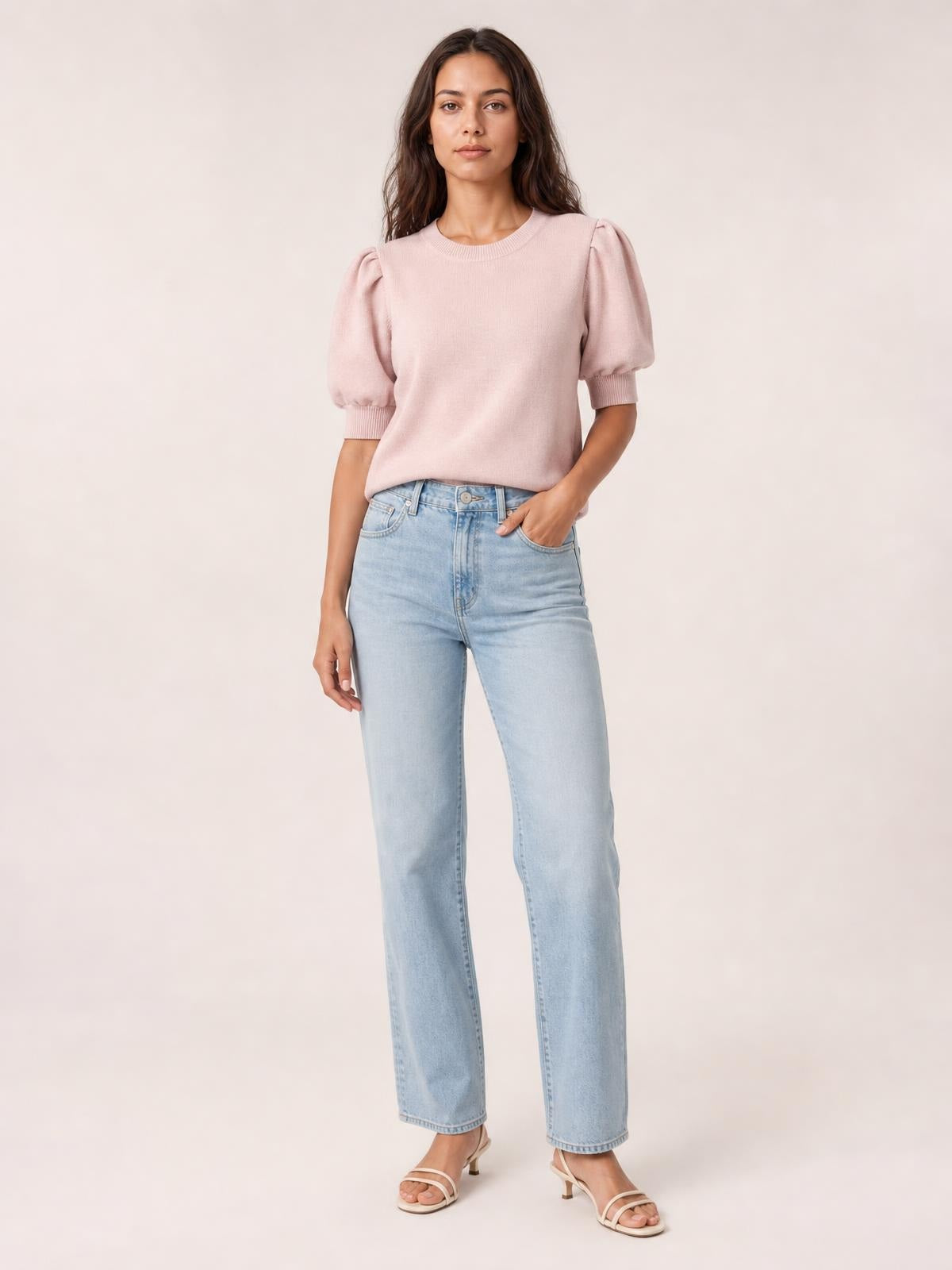 A model wears a blush pink mock neck puff sleeve sweater with a relaxed silhouette, ribbed neckline and cuffs, and one hand tucked into her jeans pocket.
