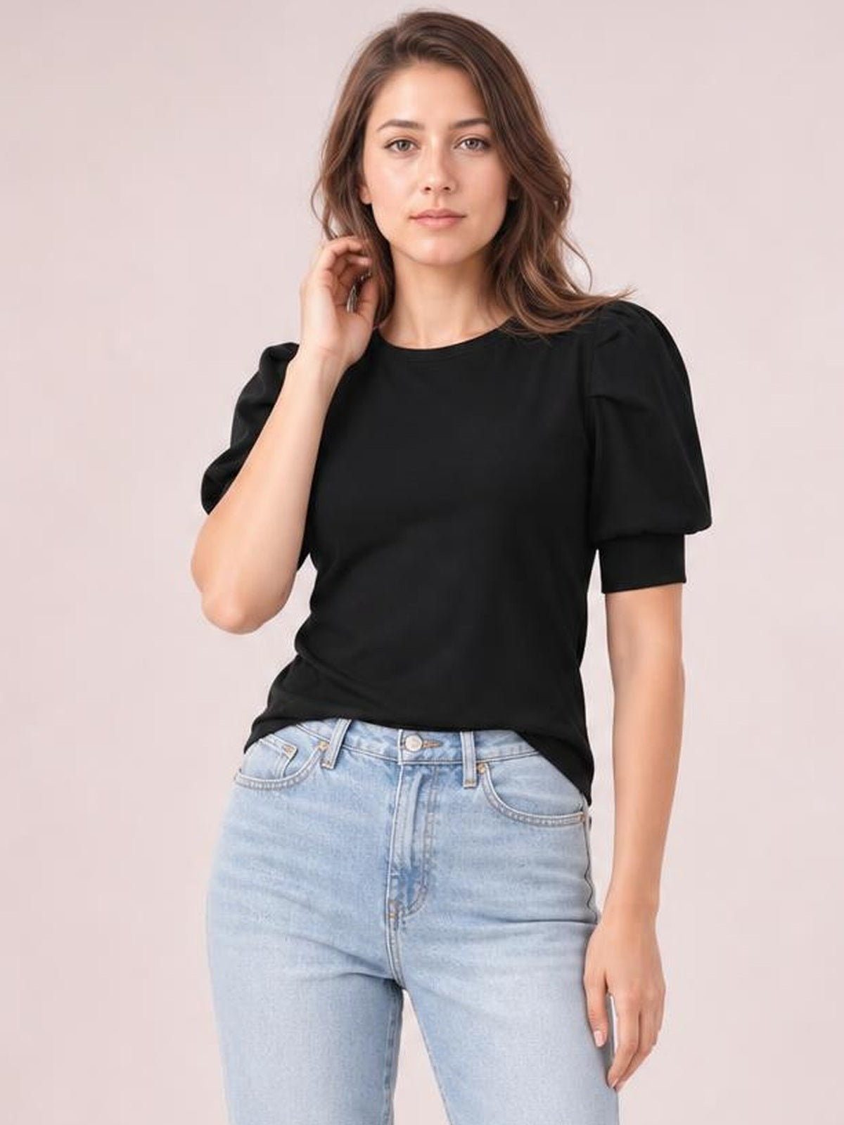 Model touches her hair while wearing a black puff sleeve sweater with a simple round neckline, short sleeves, and a relaxed straight silhouette.