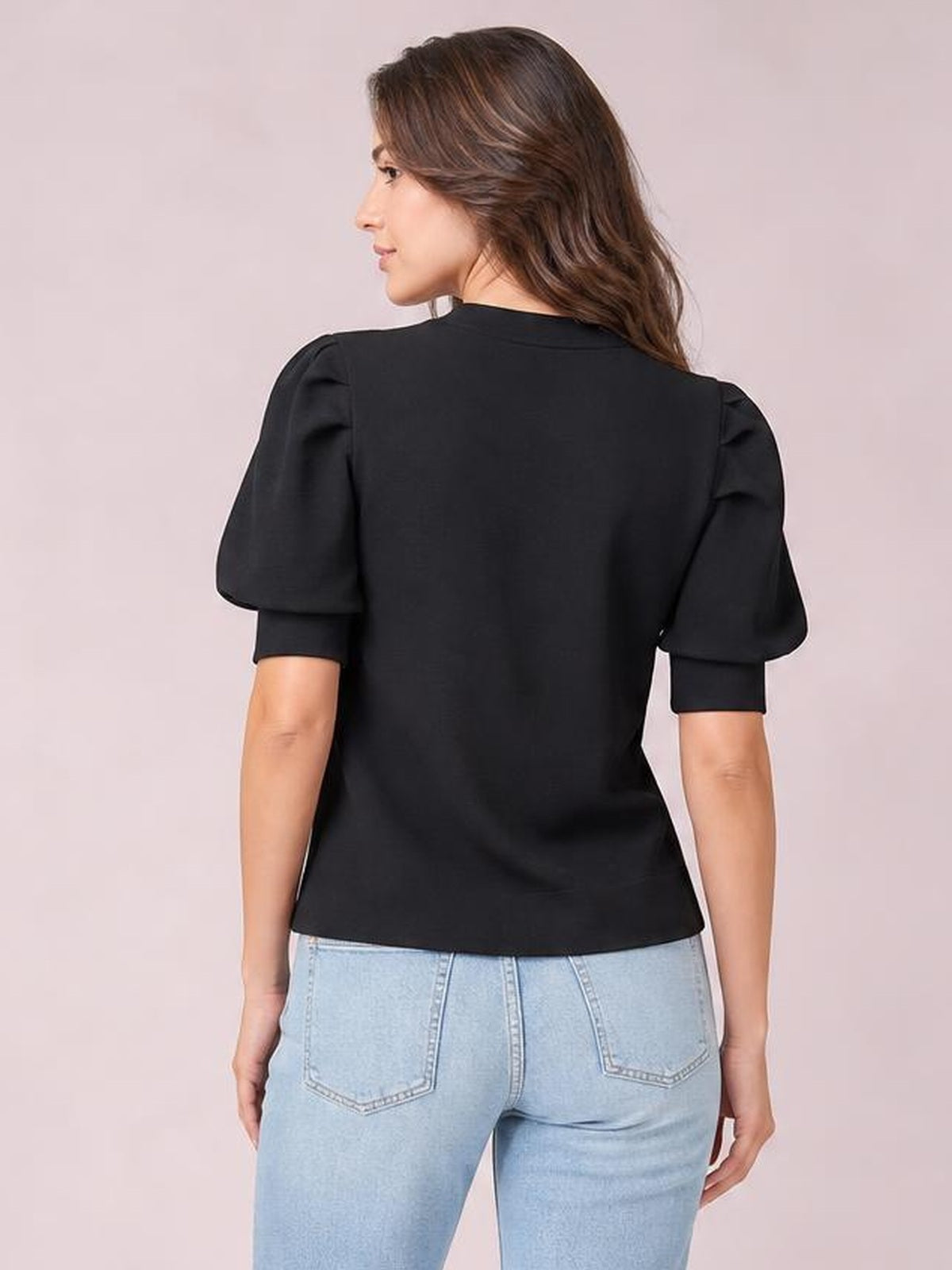 Model shown from the back in a black mock neck puff sleeve sweater with voluminous short sleeves, fitted cuffs, and a relaxed straight silhouette.