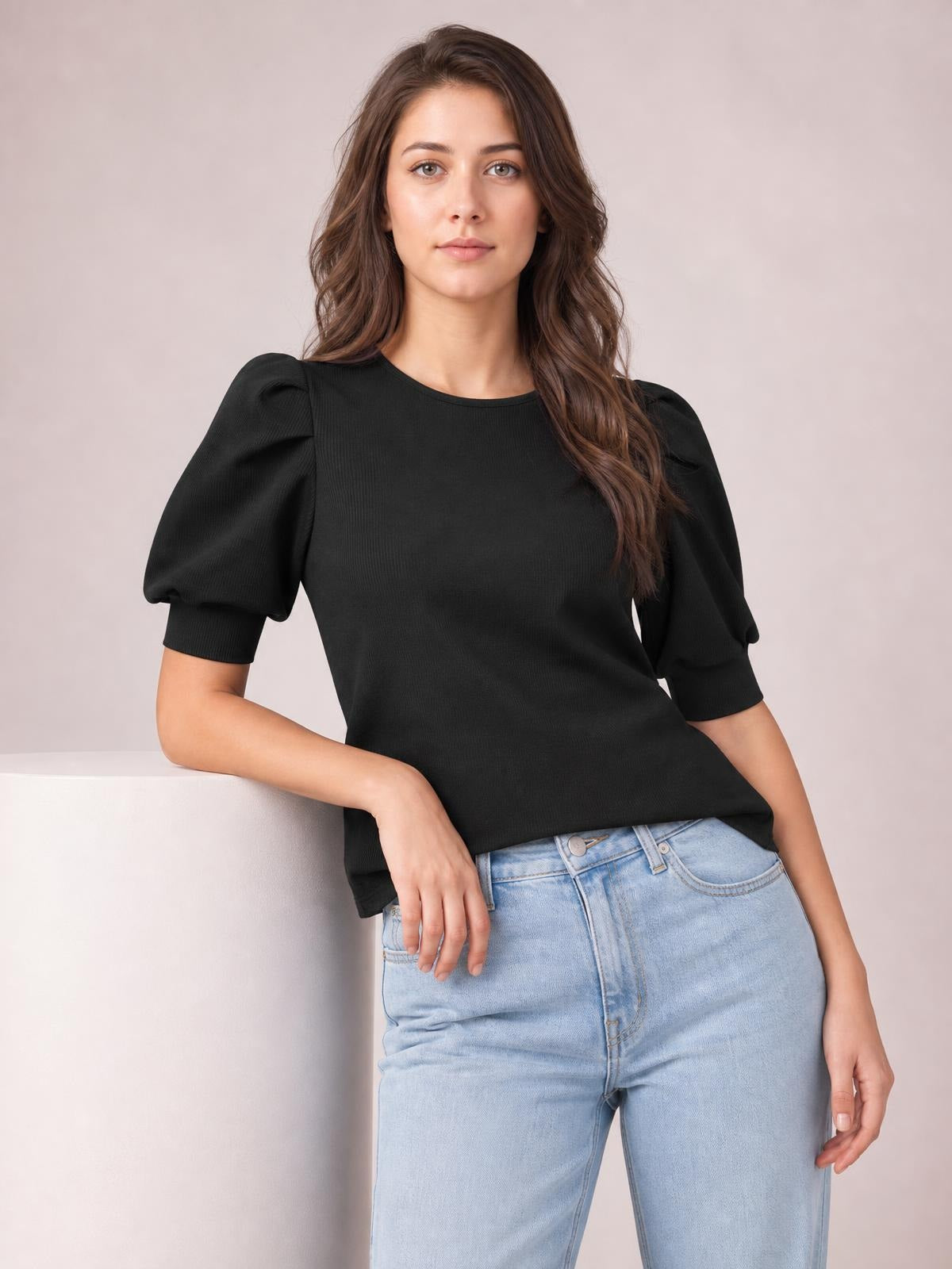 A model leans casually in a black ribbed sweater with voluminous puff sleeves, short cuffs, a fitted silhouette, and a straight hem.