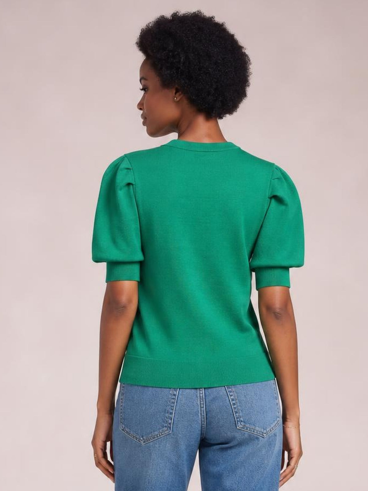 A model stands facing away in a green puff sleeve sweater with a ribbed neckline, cuffs, and hem, showing its relaxed straight silhouette.